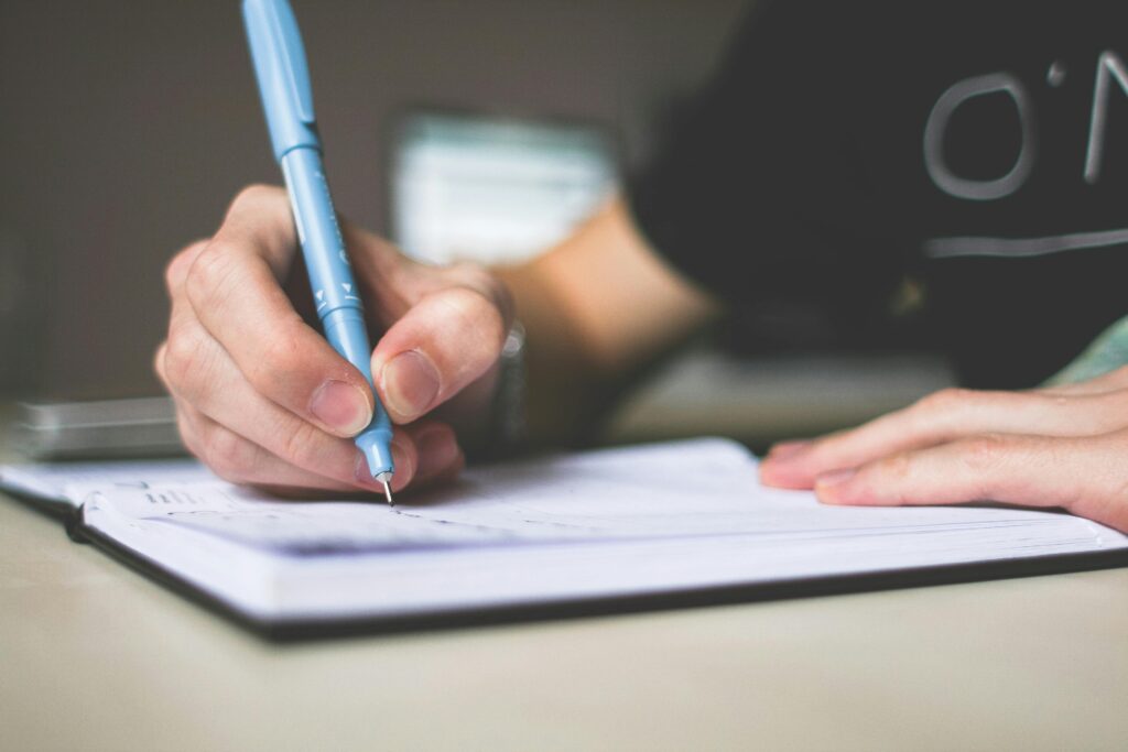 Contact us Close-up of hand writing in notebook using a blue pen, focus on creativity.