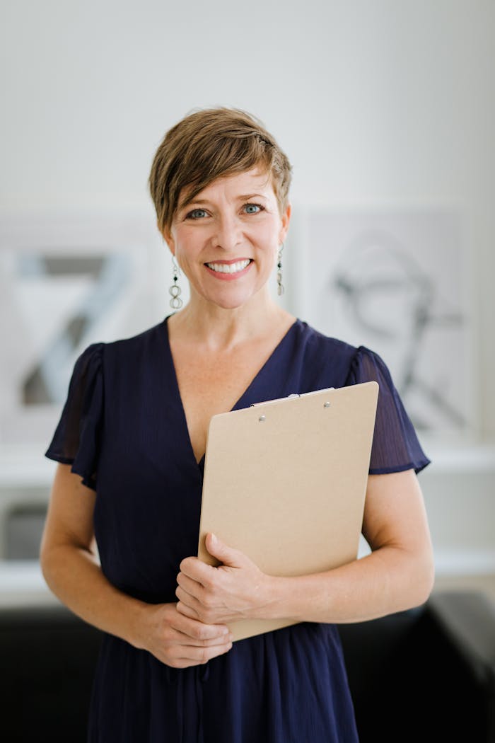 Services Smiling woman with short hair holding a clipboard, standing indoors.